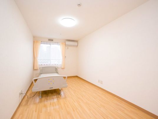 介護用ベッドが置かれたフローリングの居室には大きな窓とエアコンが付いている。