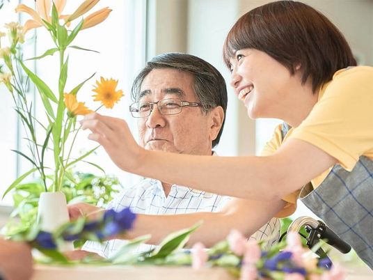 フラワーアレンジメントを楽しんでいる高齢男性とサポートをしているエプロンを付けた女性スタッフ。