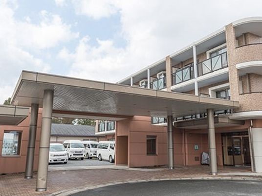 大きな窓が付いている玄関の奥には駐車場もある。ブラウン系の建物で角フロアにベランダが付いている。
