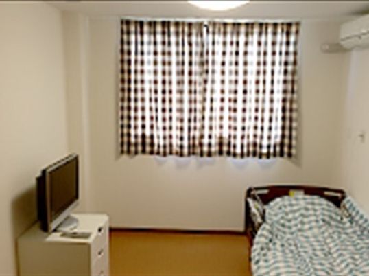 カーテン付きの大きな窓がある部屋にはエアコンや寝具付きのベッド、テレビなどが置かれている。