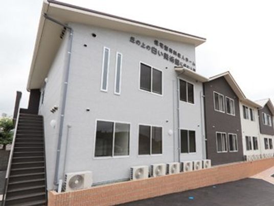 2階建ての建物はツートーンで落ち着いた雰囲気。周辺には駐車スペースがあり、階段も設置されている。