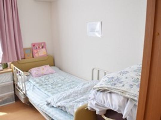 寝具付きのベッドが置かれている部屋には時計や写真も飾られ、収納ケースも置かれている。