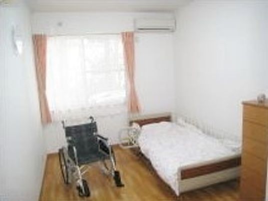 ベッドやエアコン、収納家具が設置された明るい居室には車いすも置かれている。
