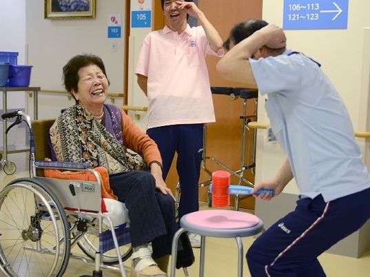 車いすの女性入居者と男性スタッフが、ピコピコハンマーで遊んでいる様子。