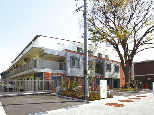 手前に街路樹がある建物の写真。３階建てで大きめなマンション風の外観