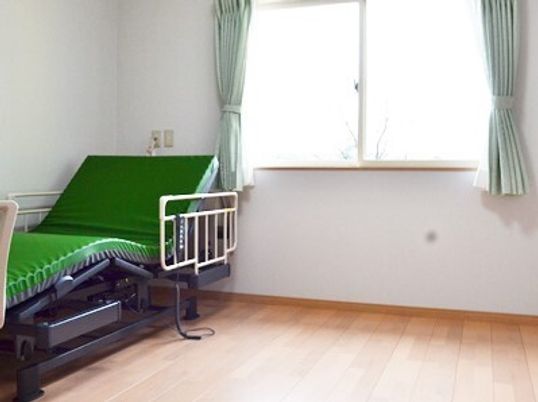 介護ベッドが設置されたフローリングの部屋には大きな窓があり、ベッドサイドには緊急通報装置がある。