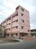 ５階建ての建物は桜色で玄関には屋根が付いている。周辺には高い建物はない。