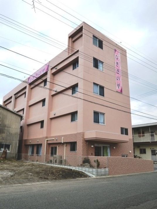 ５階建ての建物は桜色で玄関には屋根が付いている。周辺には高い建物はない。