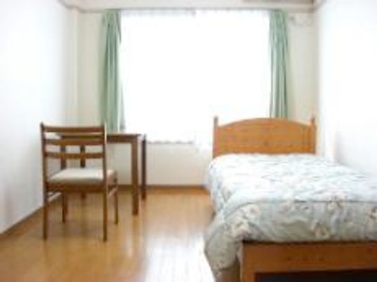 右側にベッド、左側に椅子と机が置いてある小さな部屋の様子。窓があるワンルームタイプの部屋