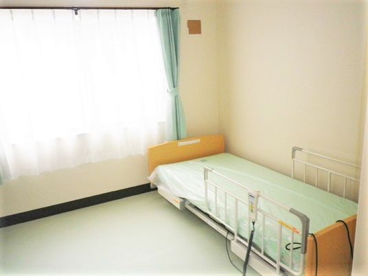 介護用ベッドと緊急コール、奥のほうに窓がある小さな部屋の様子。施設内の居室の写真