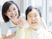 笑顔で遠くを指さしている車いすの高齢女性と一緒に笑っているエプロンを付けた若い女性スタッフ。