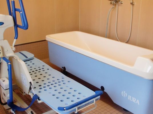 白と青の機械浴が設置された浴室には浴槽型の大きな機会とストレッチャータイプのリフトがあり、シャワーも付いている。