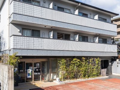 3階建ての建物は明るいグレーで敷地内には木も植えられ、駐車スペースもある。