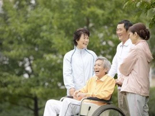 家族やスタッフと出かけている車いすの高齢者。公園のような自然豊かな場所