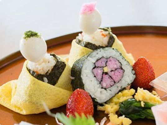 ひな人形の形をした立体的な寿司が盛られた赤い盆にはいちごやおかずなども添えられている。色鮮やかな寿司が目を引く。