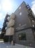 ダークグレーの4階建ての建物。側面には屋外階段とベランダが付き、外壁にはホーム名が書かれ、ロゴマークが描かれている。