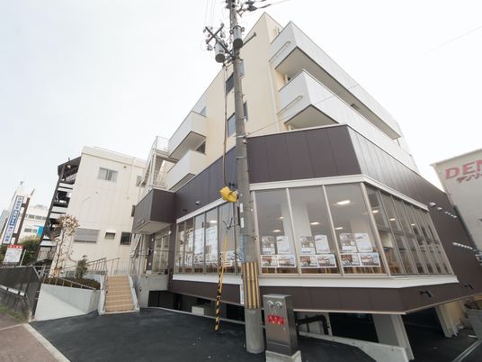 3階建ての建物は白をメインとしていて、1階部分はグレー。1階部分はガラス張りとなっていて、2階以上のフロアにはベランダが付いている。