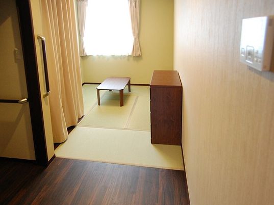 畳敷きの和室の部屋にはローテーブルやタンスが置かれ、大きな窓にはレースカーテンとカーテンが付いている。