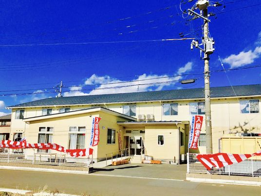 ２階建ての建物の前には平屋建ての建物があり、紅白の垂れ幕がかかっている。