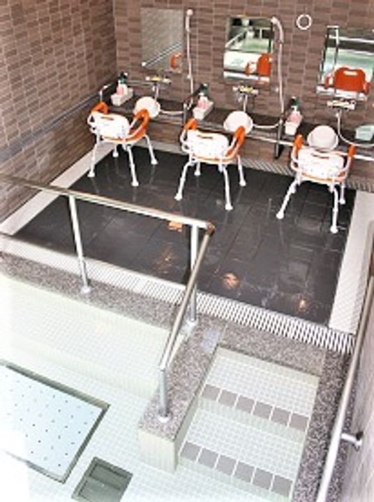 シャワーチェアが３脚並ぶ施設内の浴室。手前に手すり付きの浴槽がある