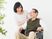 白い服を着た高齢女性と眼鏡をかけた高齢男性が寄り添い、笑顔で話している。