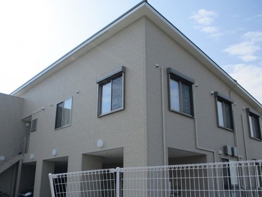 ベージュ系の２階建ての建物の周りには白いフェンスが立っていて、建物はほかにない。
