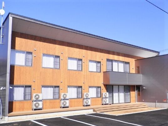ベージュの壁が印象的なグループホームの建物。手前に駐車場スペースがある