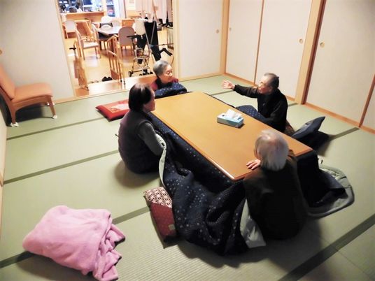 和室に置かれたこたつに集まり、熱心に話し込んでいる4名の入居者。