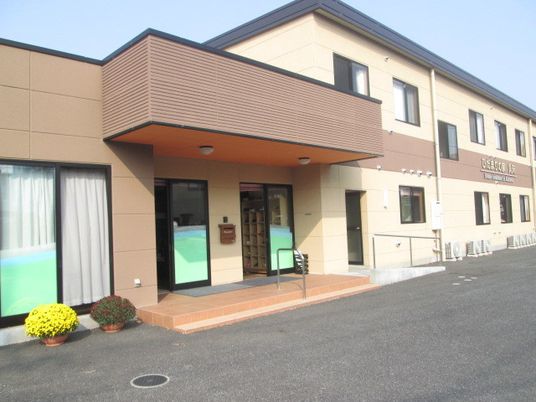 2階建ての建物はブラウン系で統一され、玄関には屋根が付き、すぐそばに季節の花が植えられた鉢が置かれている。