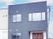 白やグレーの外壁の２階建ての建物は日当たり良好で窓がたくさん付き、玄関に屋根がある。