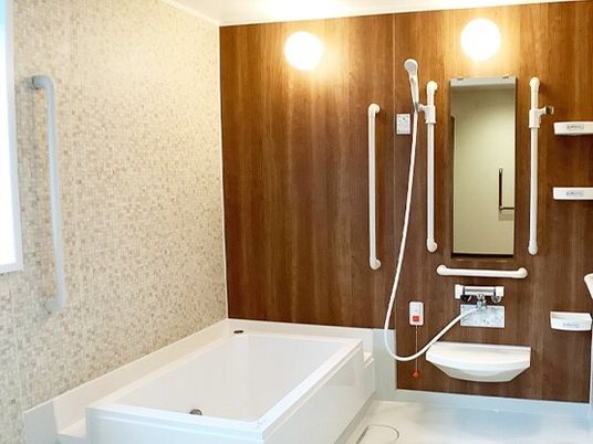 手すりがたくさん付いた一人用の浴槽が設置されている浴室にはシャワーもあり、オレンジの呼び出しボタンもある。