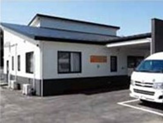白い壁にグレーの屋根といった和風の建物。すぐそばに白い車が止まっている。
