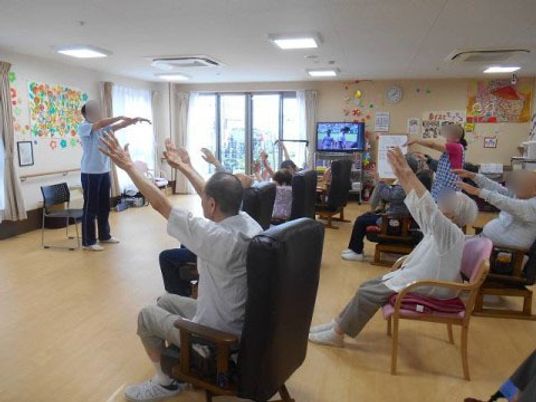 椅子に座り体操する人々
